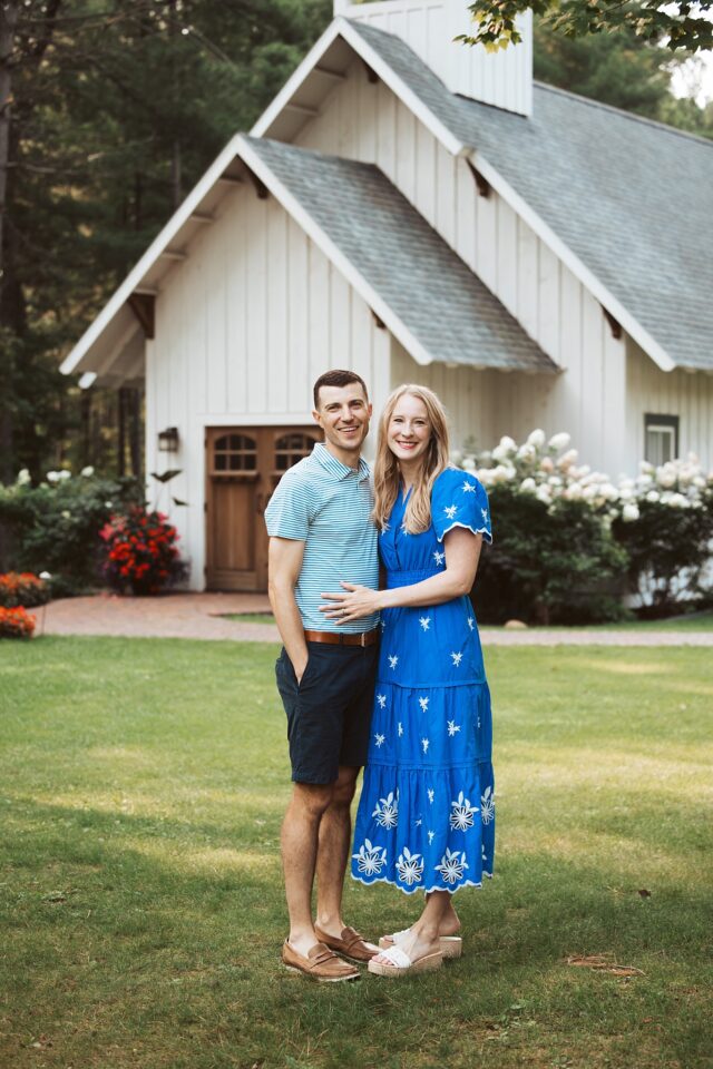 A husband and wife posing for a casual portrait in front of a white chapel at Grand View Lodge in Nisswa MN