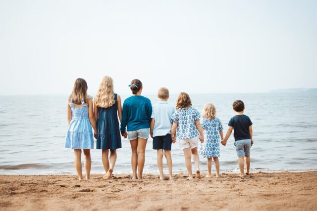 Grandchildren holding hands on the beach at Grand View Lodge in Nisswa, MN looking at Gull Lake. The children are dressed in casual blue for a family photo session at the resort.